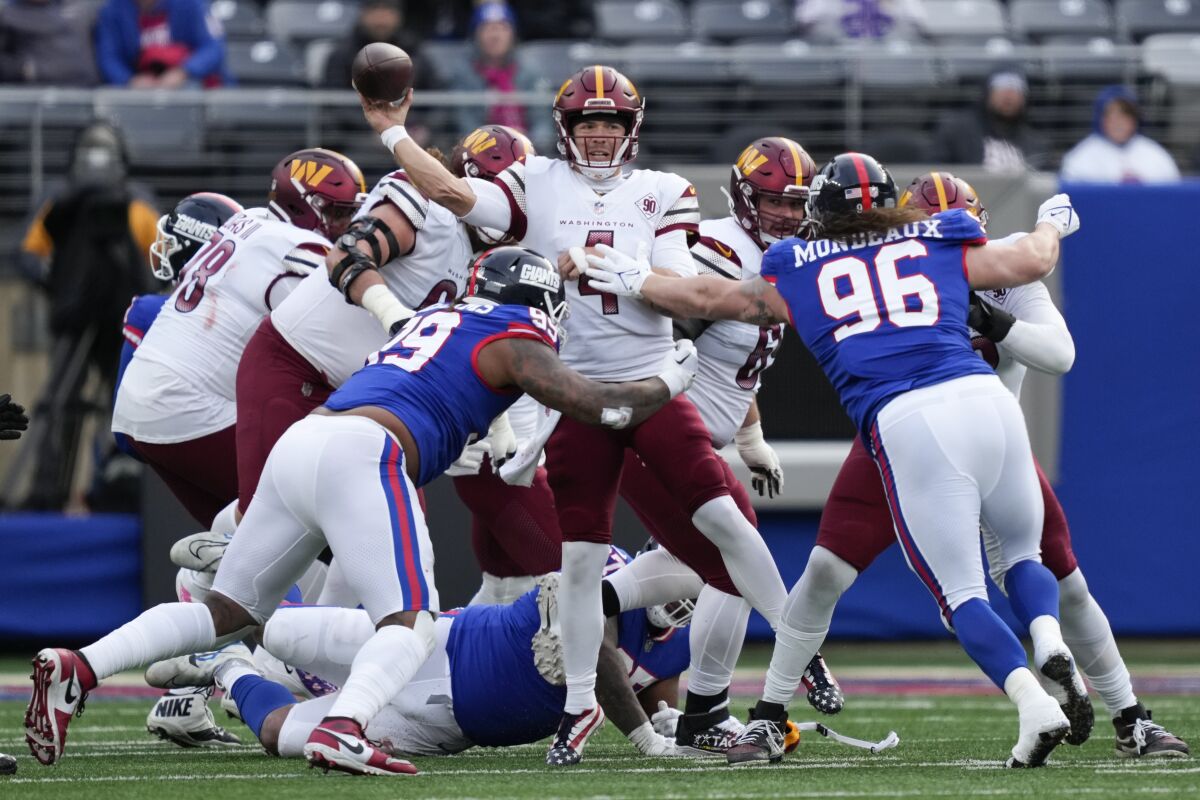 Washington Commanders quarterback Taylor Heinicke (4), center, throws under pressure from New York Giants' defenders during the second half of an NFL football game, Sunday, Dec. 4, 2022, in East Rutherford, N.J. (AP Photo/John Minchillo)