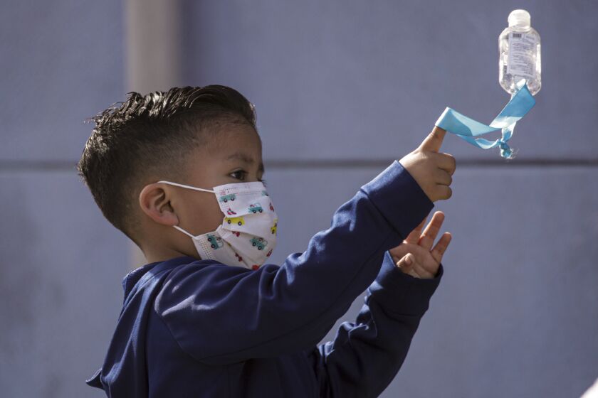 South Gate, CA - April 15: Leighton Sonco, 5, in face mask and hand sanitizer bottle hanging, plays on the reopening day of Madison Elementary School on Thursday, April 15, 2021 in South Gate, CA.(Irfan Khan / Los Angeles Times)