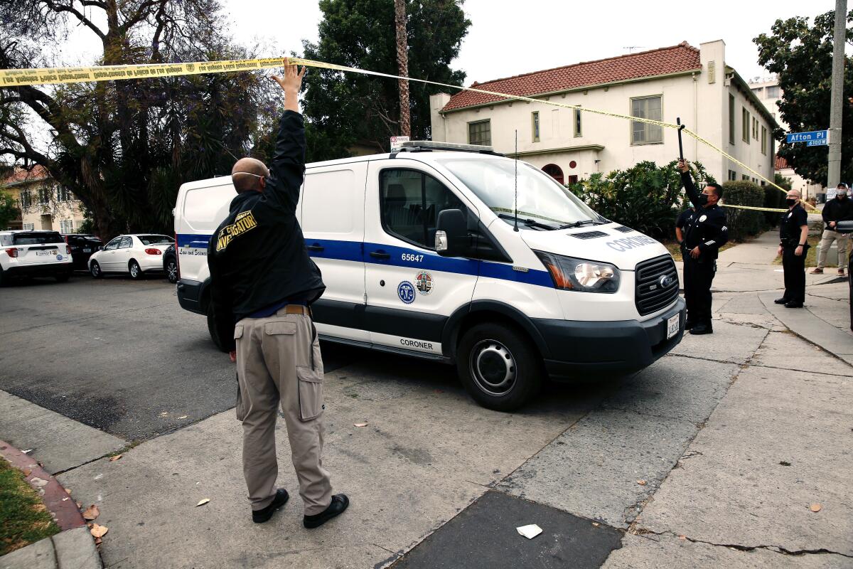 Officers hold up crime scene tape as a van that says "Coroner" drives under it.
