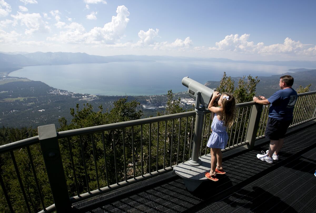 FILE - In this Aug. 8, 2017, file photo, Lilyana Allen, of Guam, uses a telescope to view Lake Tahoe from an observation platform at the Heavenly Mountain Resort during a family visit to South Lake Tahoe, Calif. The COVID-19 pandemic helped expose the growing vulnerability of Lake Tahoe's increasingly tourism-dependent economy as housing costs balloon, year-round residency declines and more workers commute from afar or seek jobs elsewhere, a new report says. (AP Photo/Rich Pedroncelli, File)
