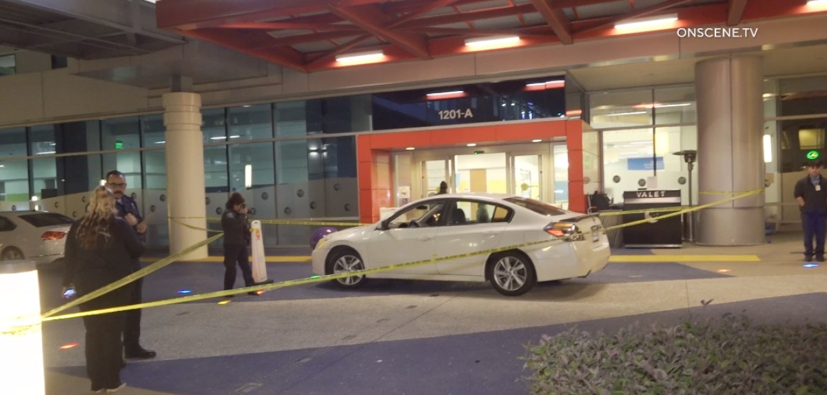 A car is surrounded by yellow police tape in front of a hospital emergency room entrance.