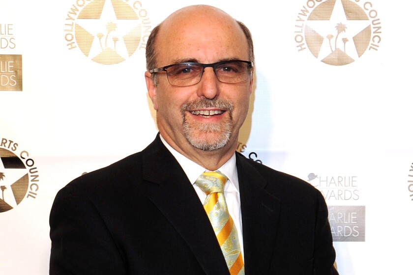 A balding man in glasses and a dark suit smiles