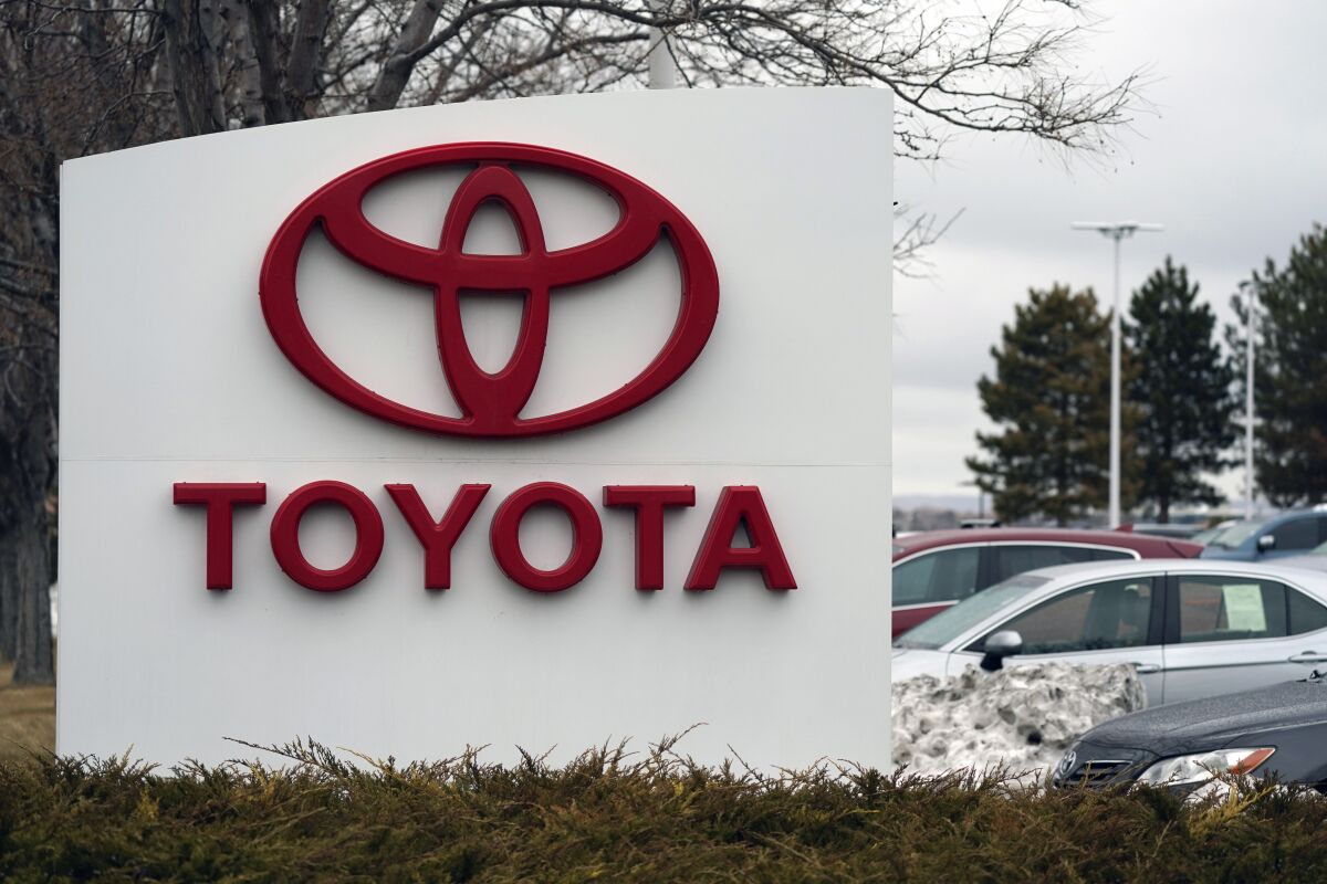 The Toyota logo in red capital letters with cars parked behind it.