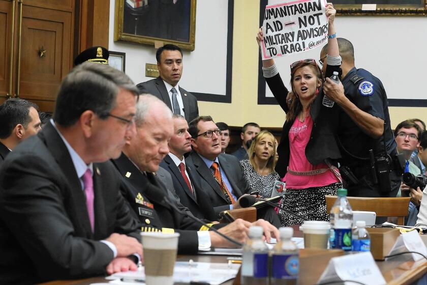 A demonstrator expresses her views as Defense Secretary Ashton Carter, left, and Martin Dempsey, chairman of the Joint Chiefs of Staff testify before the House Armed Services Committee on Capitol Hill.
