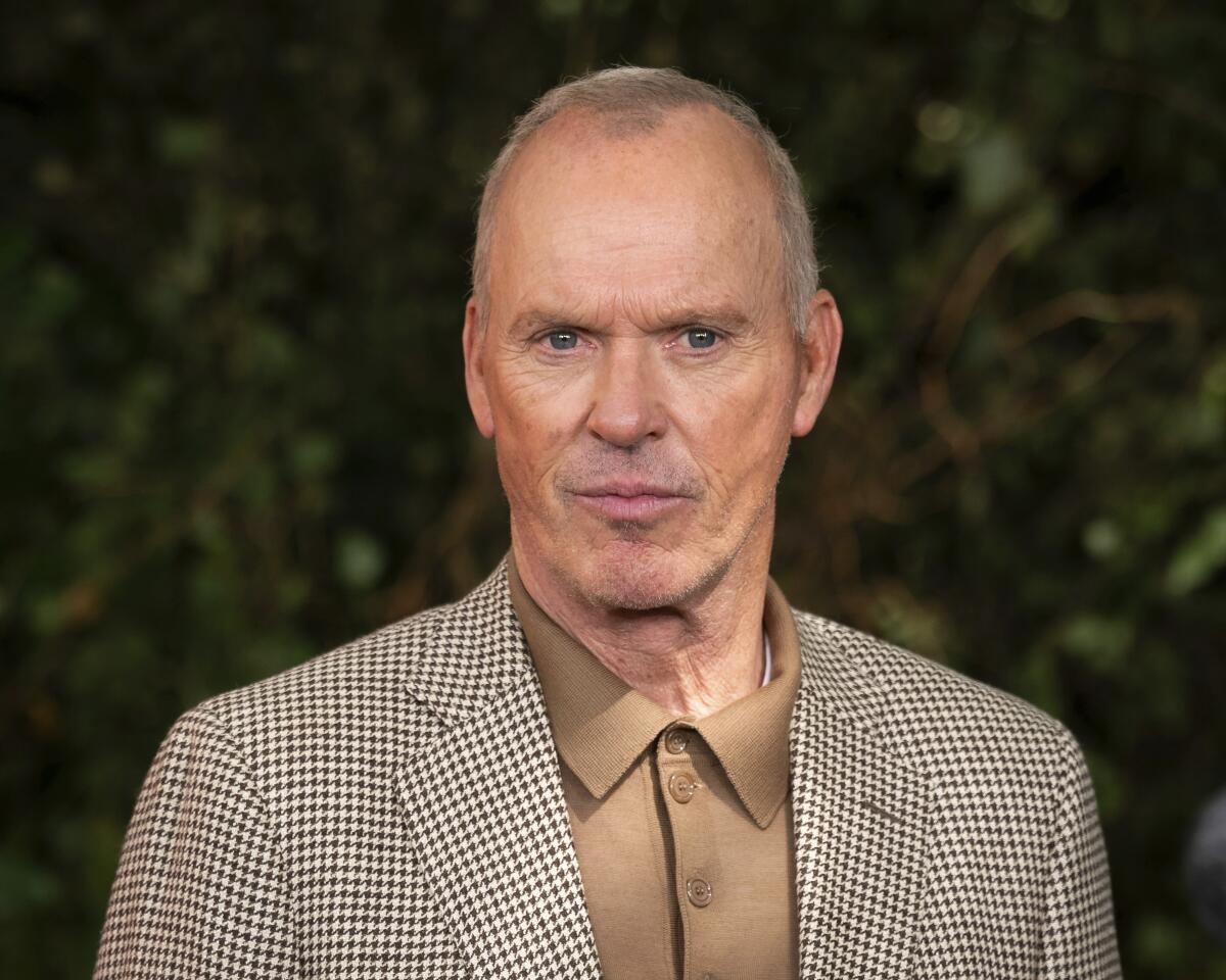 Michael Keaton poses for photographers in a tan polo and brown houndstooth blazer