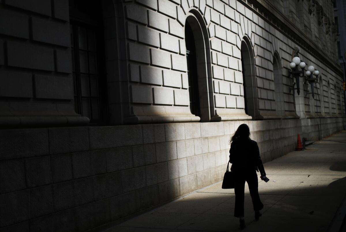 A pedestrian is silhouetted against a ray of sunlight hitting a building.