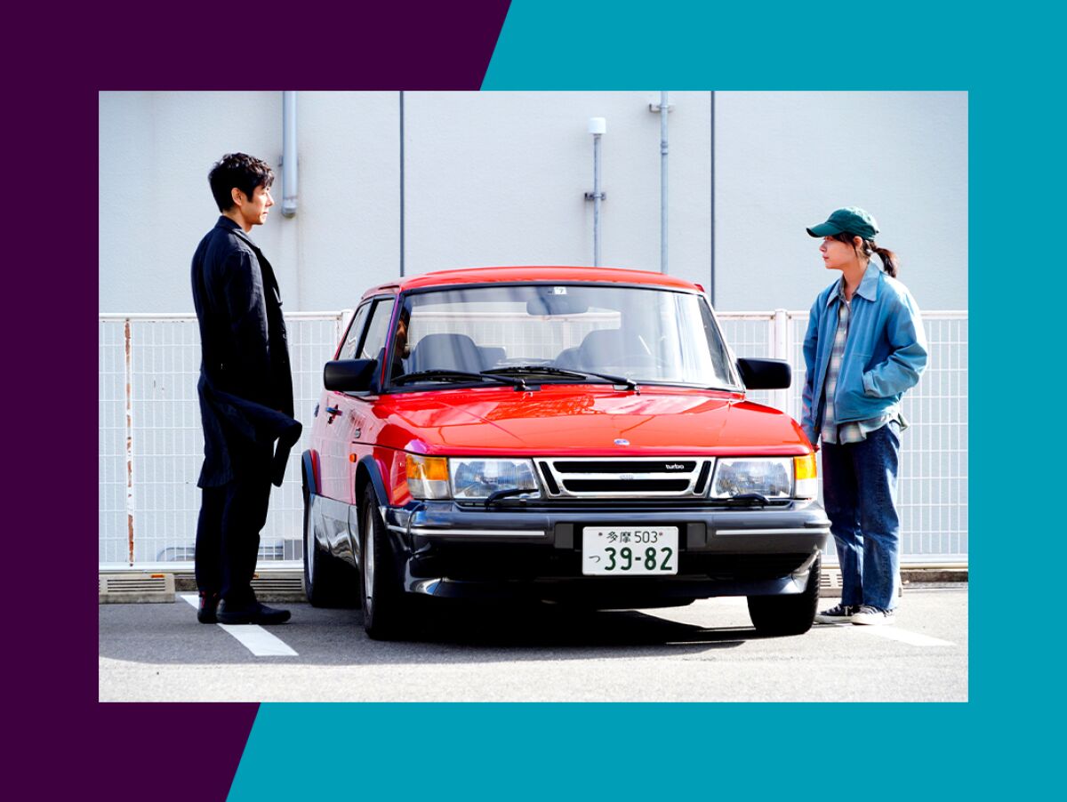A man and a woman stand on either side of a car in a scene from “Drive My Car.”