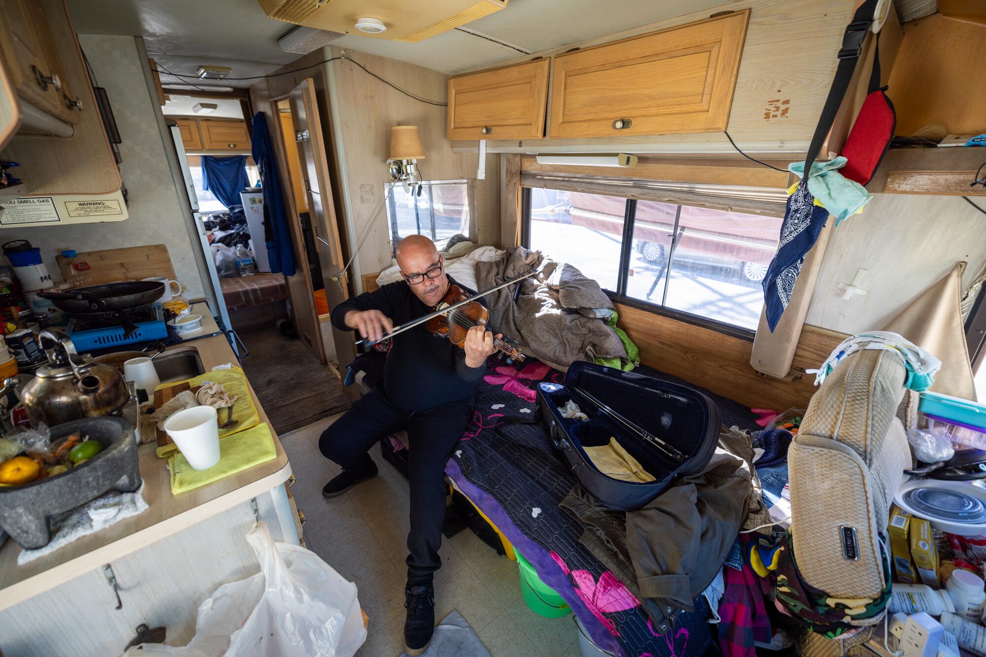 A man plays a violin in an RV.