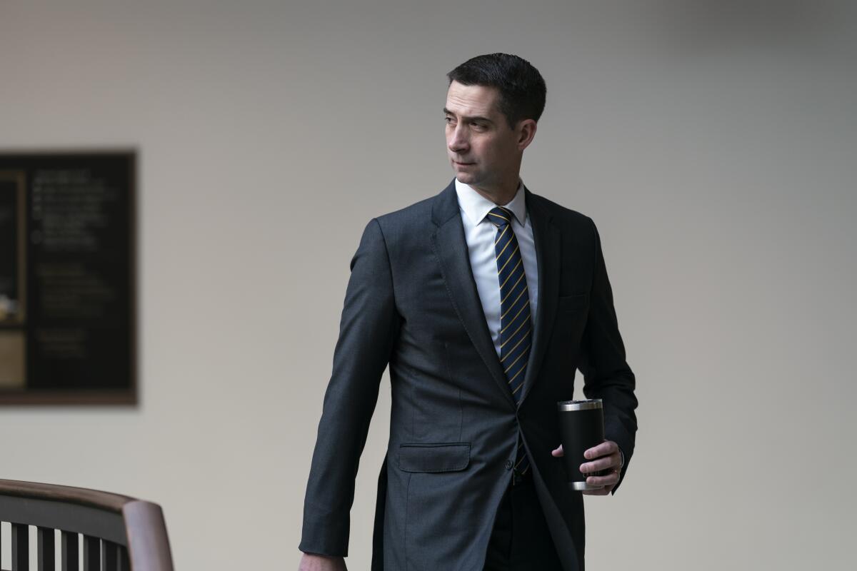 A man in  a suit is holding a beverage cup and while standing.
