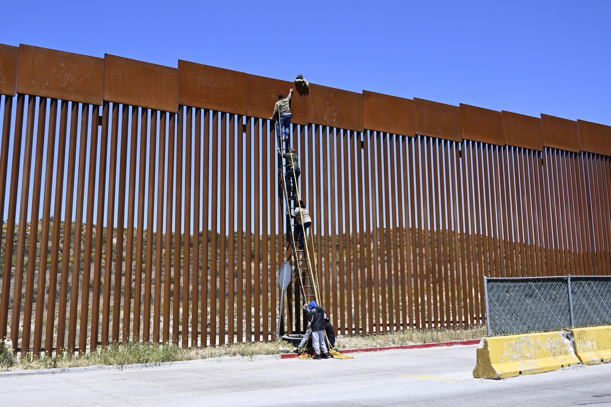 A Border Patrol agent stands in front of the 30-foot border barrier.