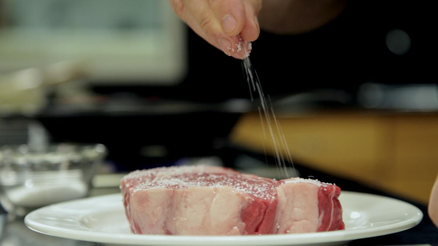 Chef David LeFevre generously seasons the rib-eye steak with salt and pepper in the Los Angeles Times Test Kitchen.