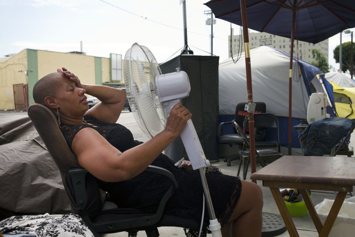 Stephanie Williams, 53, cools off using a fan running on a portable battery on Thursday, Sept. 10, 2015, in the skid row area of Los Angeles. More heat is forecast for the first weekend of fall.