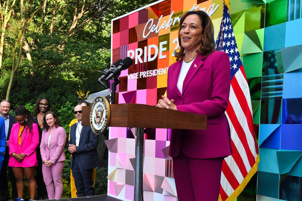 A woman in a deep pink pantsuit speaks at a lectern bearing a seal of office