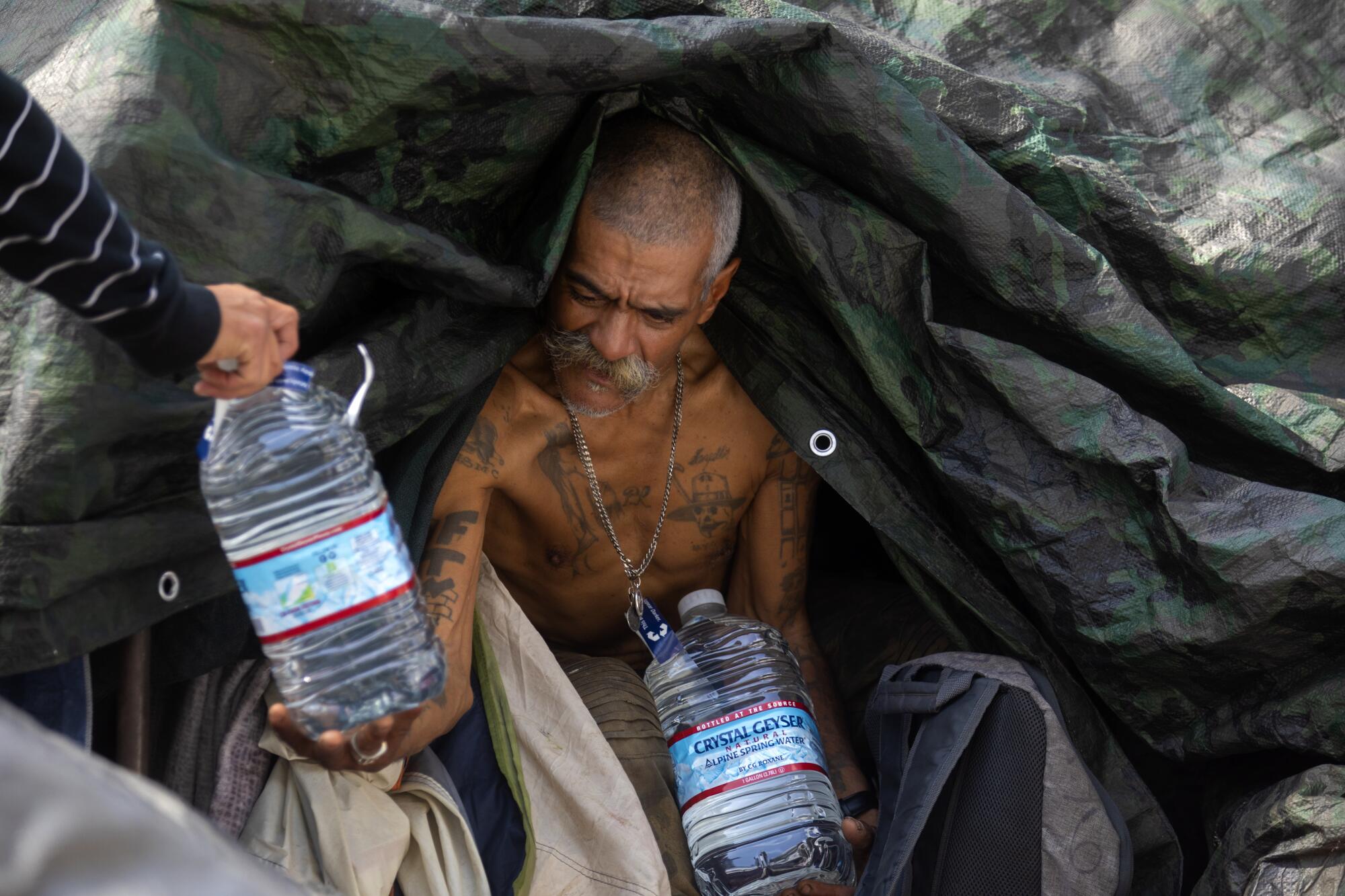 A man holds bottled water in his tent.