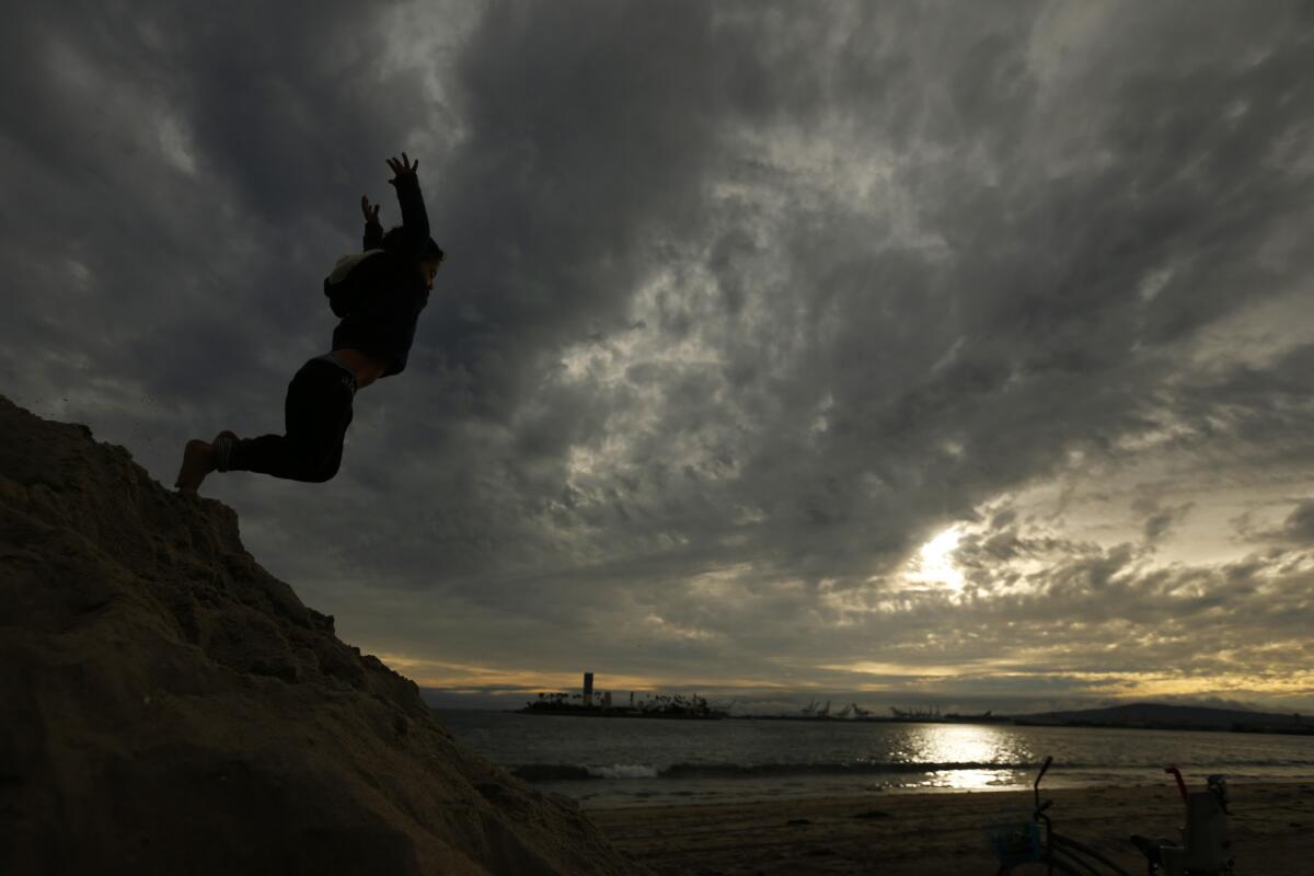 Gianny Carvajal, 4, jumps off a hill of sand while visting the beach with his parents and brother as clouds roll over Long Beach on Saturday afternoon.