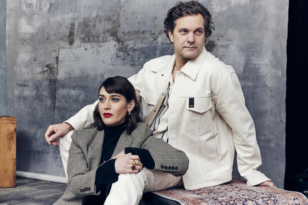 Lizzy Caplan leans on Joshua Jackson's leg as they pose for a portrait.