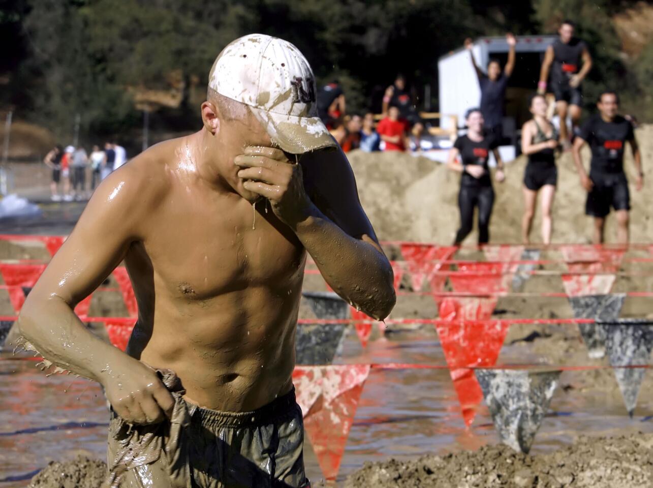 A participant clears mud from his eyes after the mud crawl station of the Gladiator Rock 'n Run.