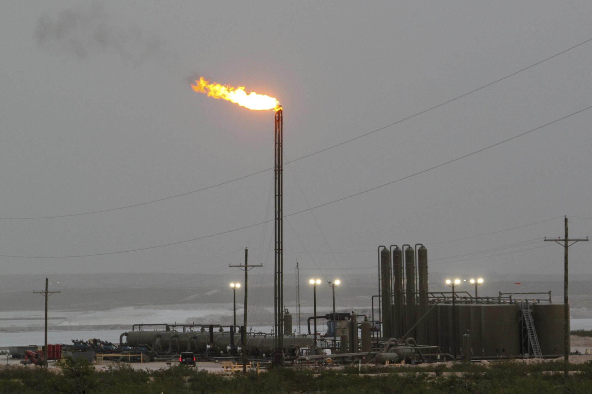 Strong winds kick up dust as a facility in the Permian Basin flares natural gas