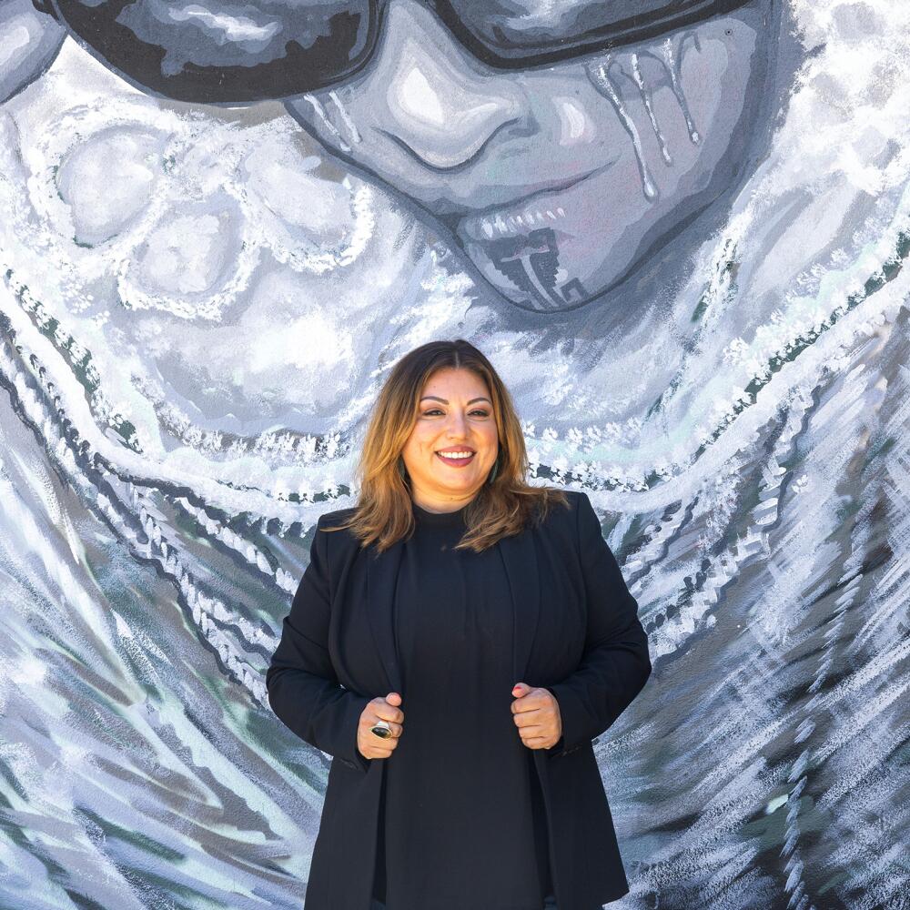 A woman stands in front of a mural.