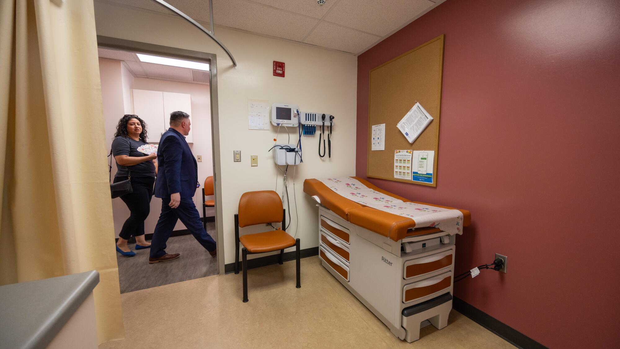 People walk past an examination room in a clinic.