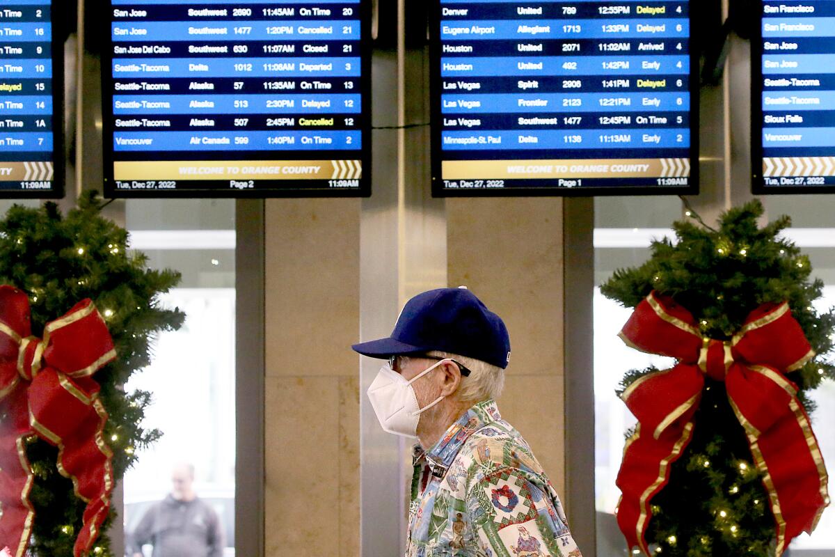 A man wearing a KN-95 mask walks near arrivals monitors at John Wayne Airport.