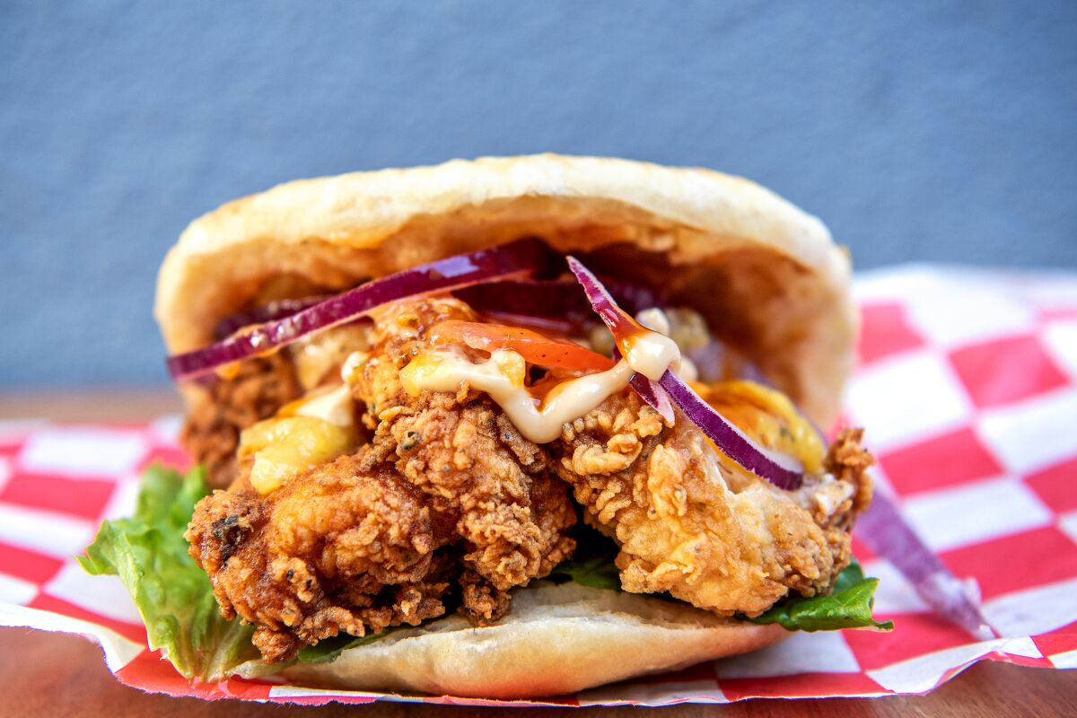 Fried chicken, onion, tomato and sauce spill out of a bun.