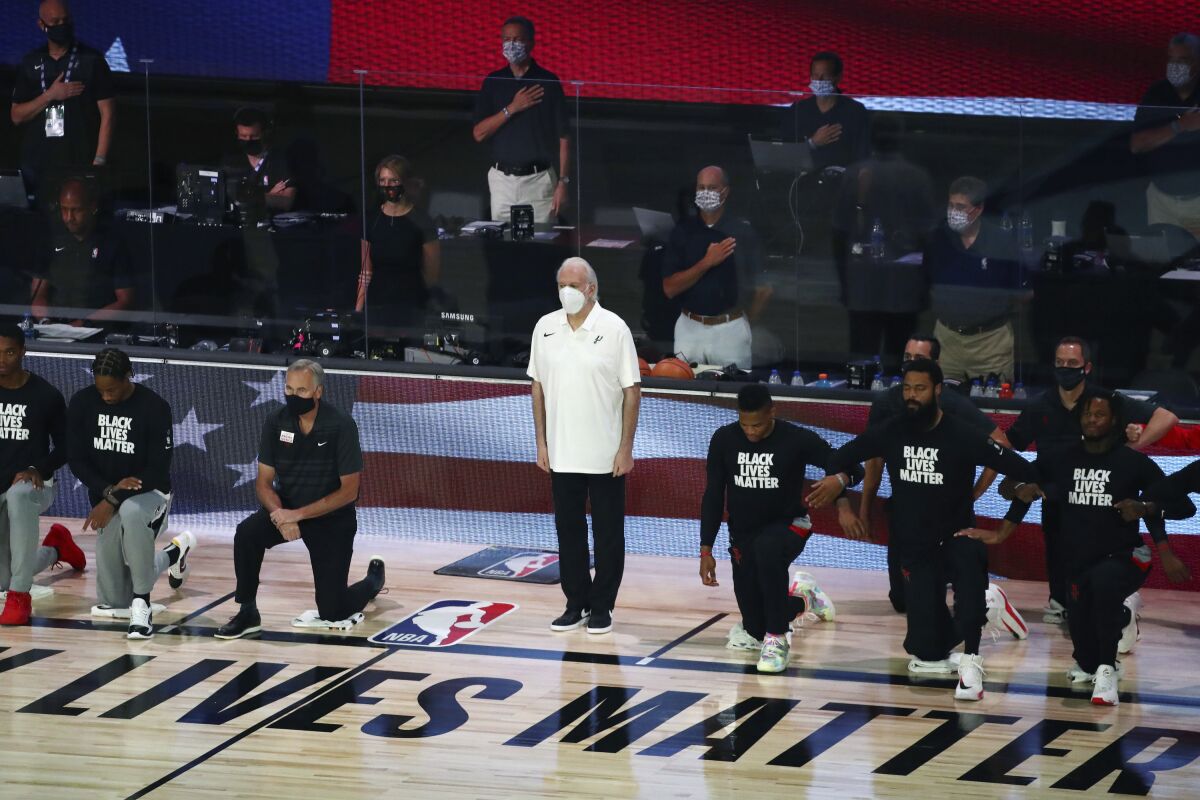 San Antonio Spurs head coach Gregg Popovich, standing at center, wears a mask while players kneel before an NBA basketball game against the Houston Rockets, Tuesday, Aug. 11, 2020, in Lake Buena Vista, Fla. (Kim Klement/Pool Photo via AP)
