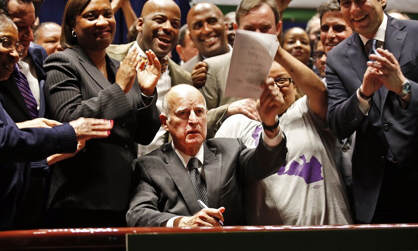 Gov. Jerry Brown holds the signed copy of the minimum wage bill at the Ronald Reagan State Building in Los Angeles.