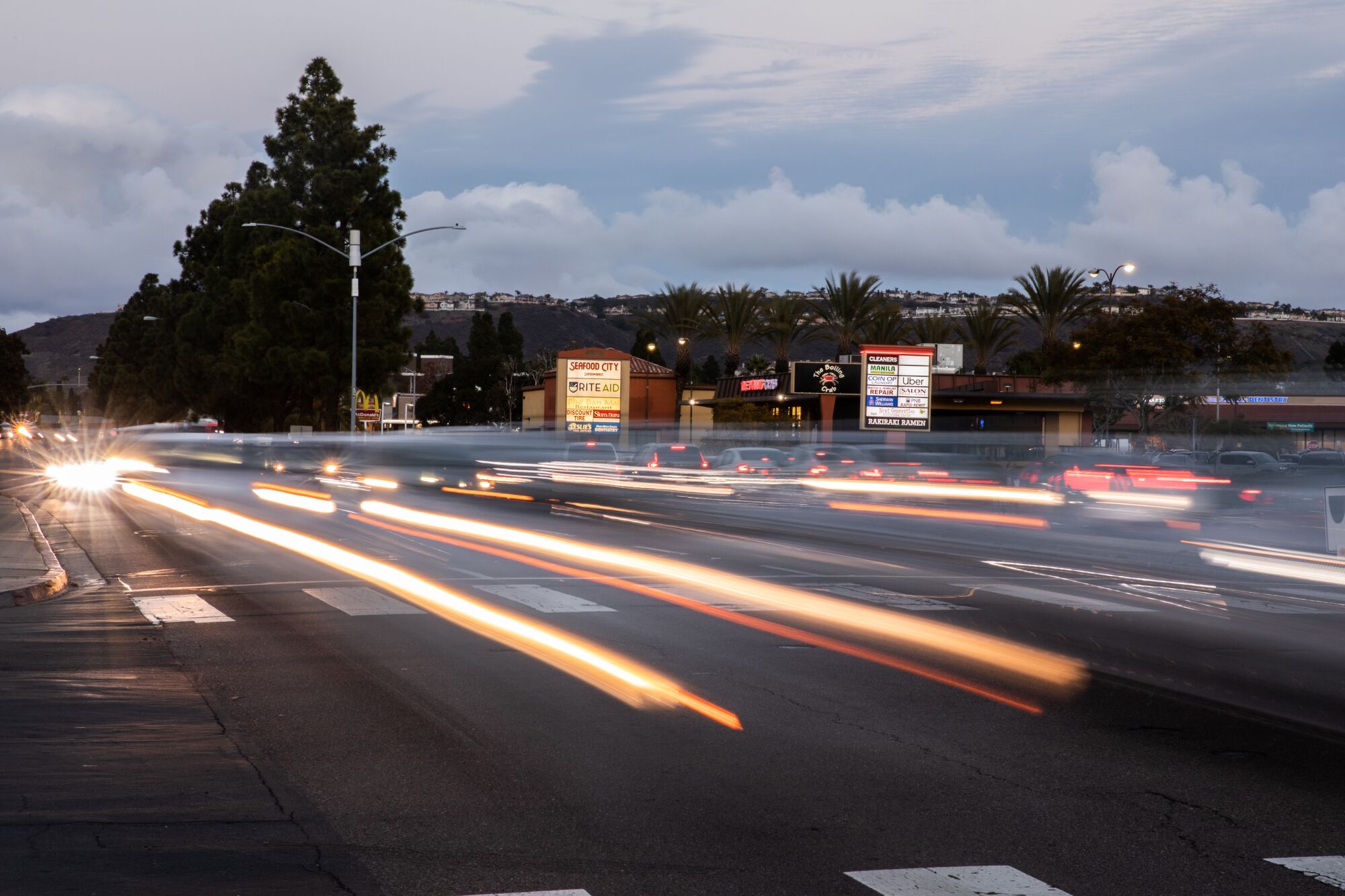 A long-exposure photo of traffic on a busy road at sunset shows cars' headlights and brake lights as red and white streaks.