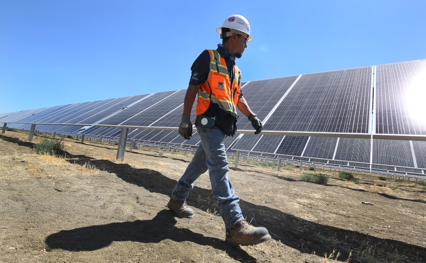 A person in an orange vest walks past solar panels outdoors.