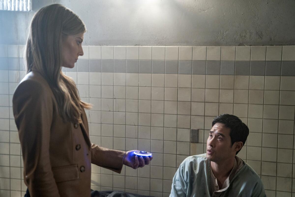 woman standing up holds up a device to a man sitting down in a room with tiled walls