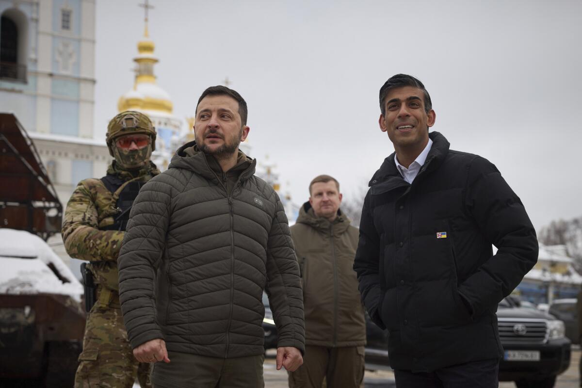 Ukrainian President Volodymyr Zelensky and British Prime Minister Rishi Sunak stand outside in coats.