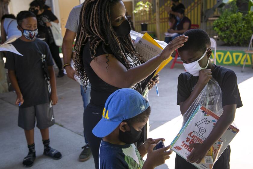 LOS ANGELES, CA - AUGUST 18: Tunette Powell, 34, rests her hand on her son Joah Powell's, 9, head as they wait to pick up school supplies during the first day of school at Baldwin Hills Elementary School on Tuesday, Aug. 18, 2020 in Los Angeles, CA. (Josie Norris / Los Angeles Times)