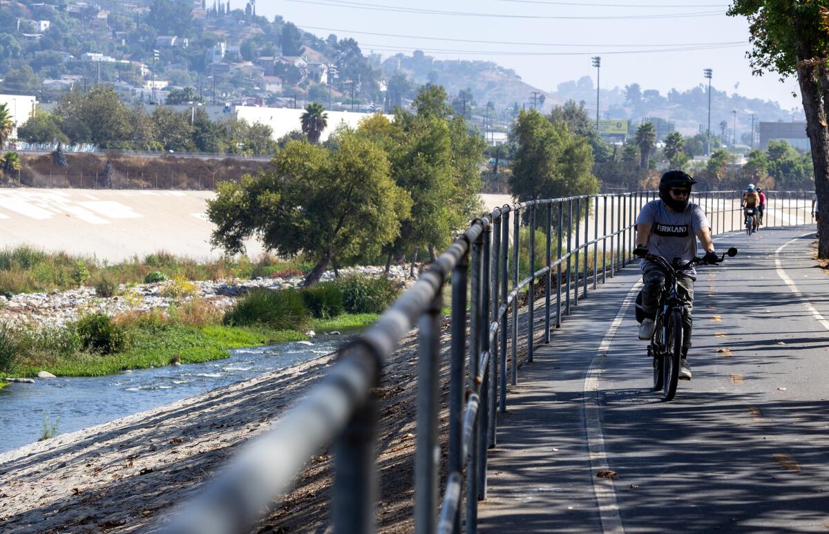 People ride bicycles on a path next to a river.