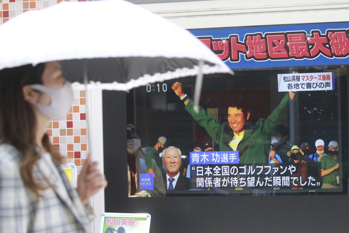 People walk past the tv screen showing the image of Japanese golfer Hideki Matsuyama in a news channel in Tokyo, Monday, April 12, 2021. From Japan's prime minister on down, the country celebrated Matsuyama's victory in the Masters — the first Japanese to win at Augusta National and wear the famous green jacket.(AP Photo/Koji Sasahara)