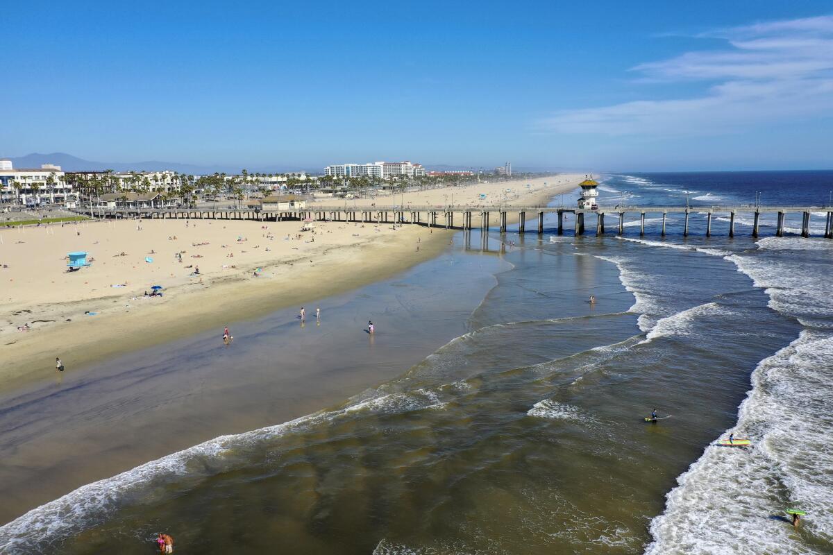 La gente disfruta de la temperatura veraniega el miércoles cerca del muelle cerrado de Huntington Beach. Se esperaba una multitud mucho mayor este fin de semana en el condado de Orange, pero no en el condado de Los Ángeles, que mantiene sus playas cerradas.