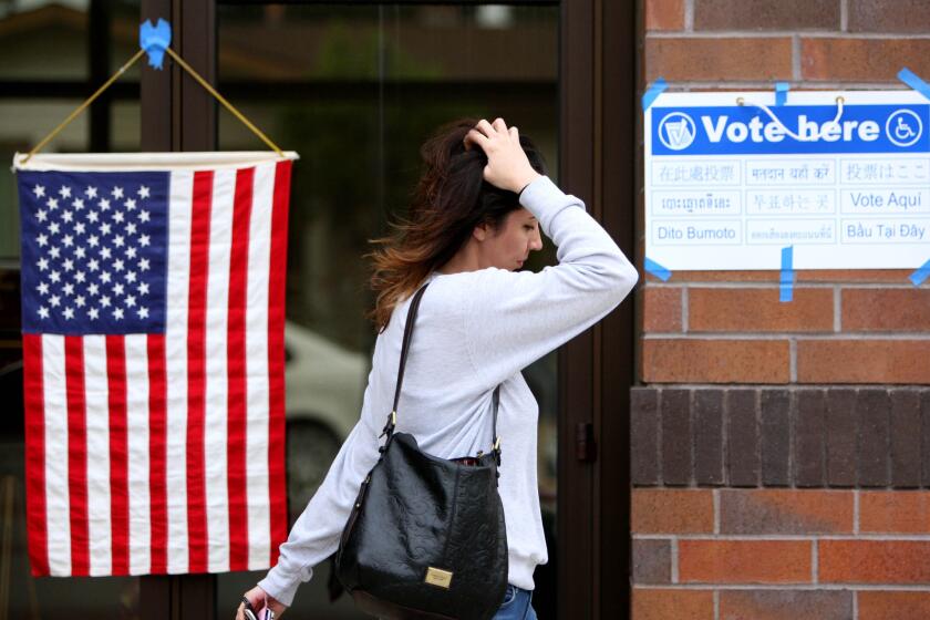A woman fixes her hair as she passes an American flag and a sign that says "Vote Here" after casting her vote at Fire Station 21 in Glendale on election day, Tuesday, June 7, 2016.
