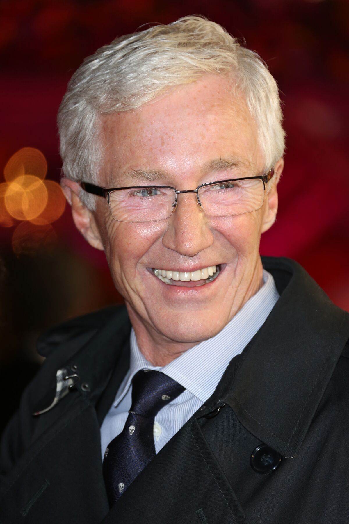 A man with white hair and glasses in a suit smiling