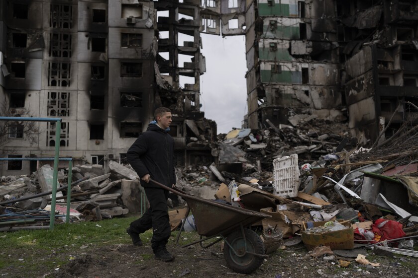 A young man pushes a wheelbarrow in front of a destroyed apartment building in the town of Borodyanka, Ukraine, on Sunday, April 10, 2022. (AP Photo/Petros Giannakouris)