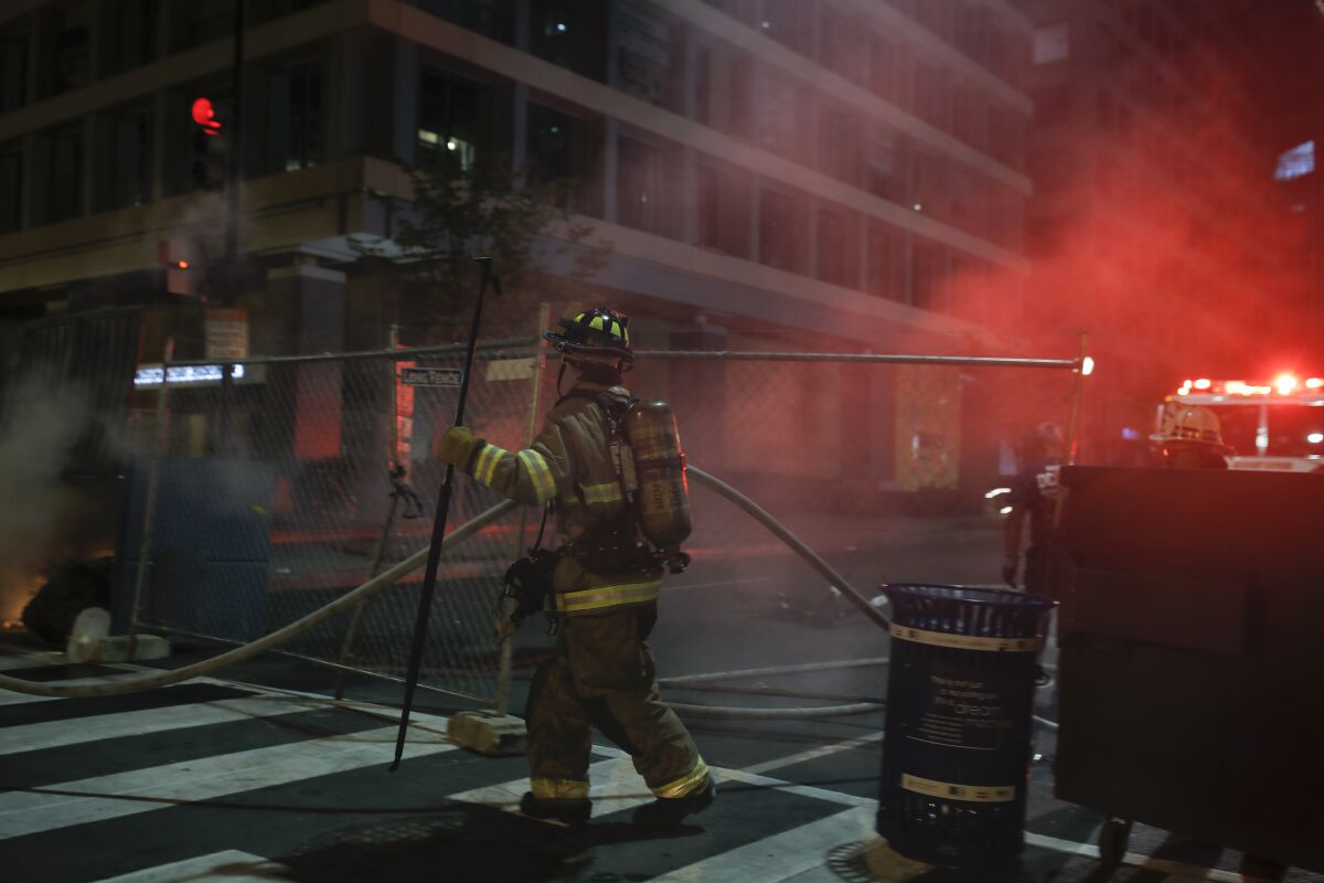 Firefighters put out a dumpster fire as protesters and police gather at Lafayette Park.