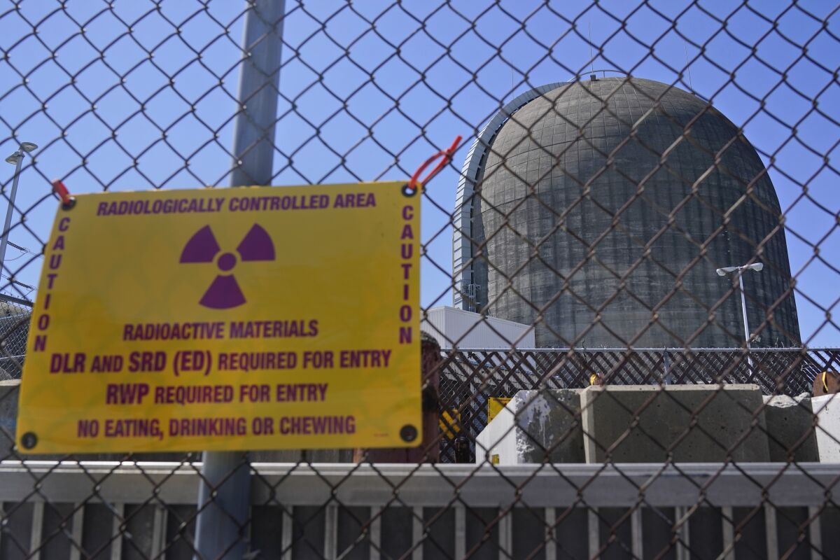 FILE - A sign on a fence warns of radioactive materials at a containment building housing a nuclear reactor at the Indian Point nuclear power plant in Buchanan, N.Y., on April 26, 2021. U.S. regulators say they need more time to wrap up a final safety report and make a decision on whether to license a multibillion-dollar project meant to temporarily store tons of spent fuel from commercial nuclear power plants around the nation. The Nuclear Regulatory Commission issued a new schedule Monday, March 20, 2023, citing unforeseen staffing constraints. (AP Photo/Seth Wenig, File)