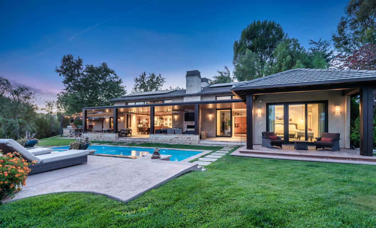 Exterior of the house with a nearby pool and grassy area with trees in the background.