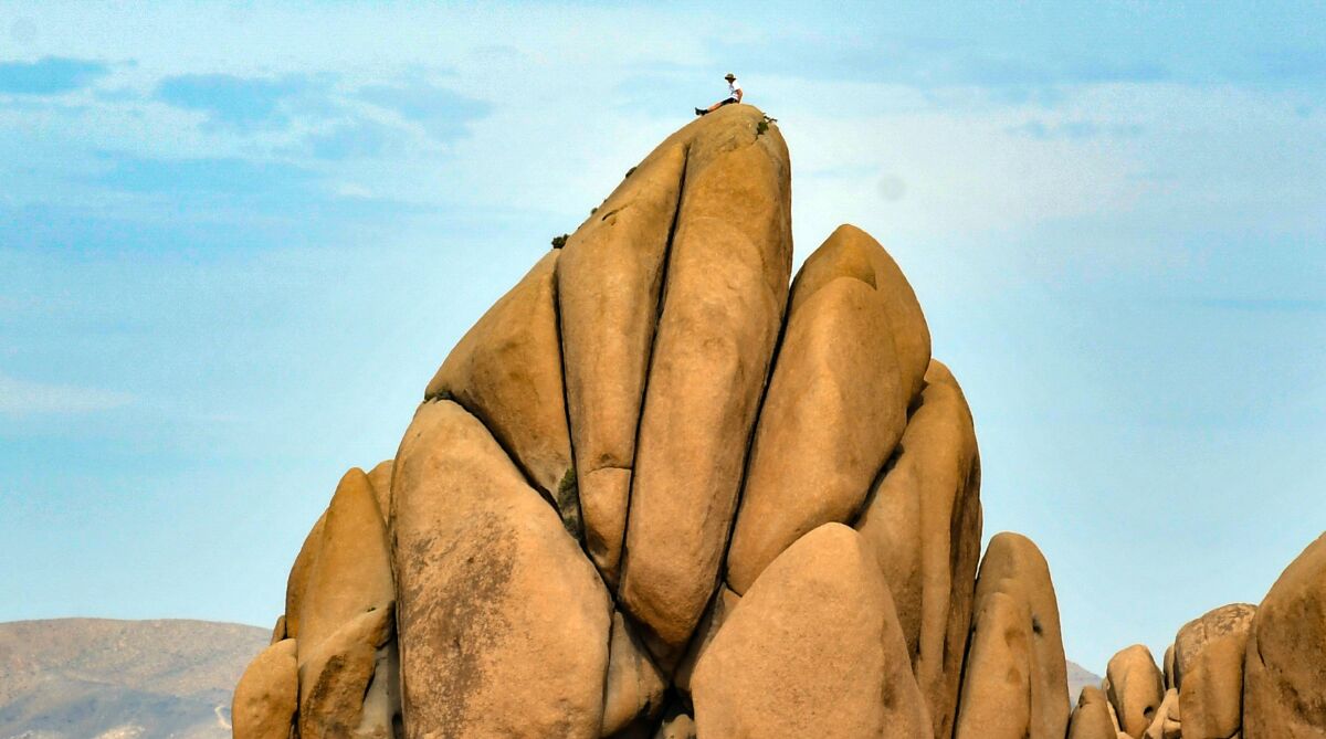 A seated climber looks tiny atop massive boulders.
