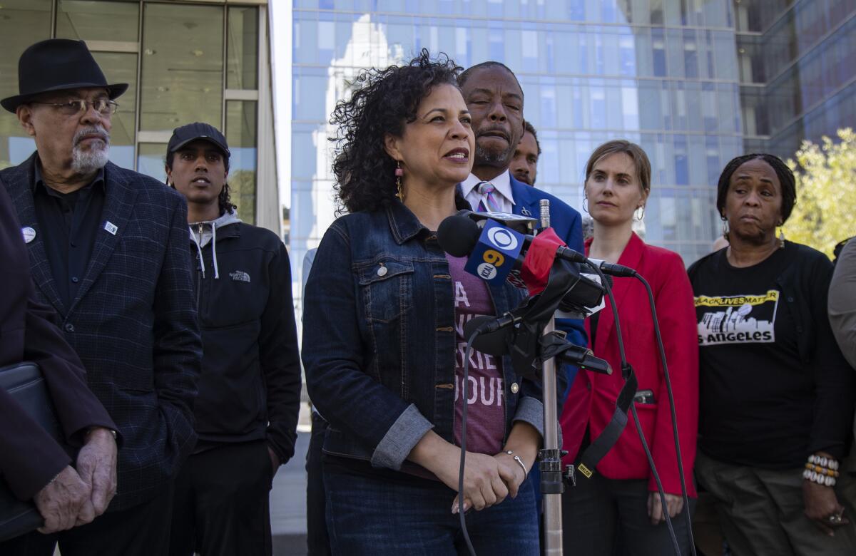 Melina Abdullah speaks into news microphones with attorneys and activists standing behind her