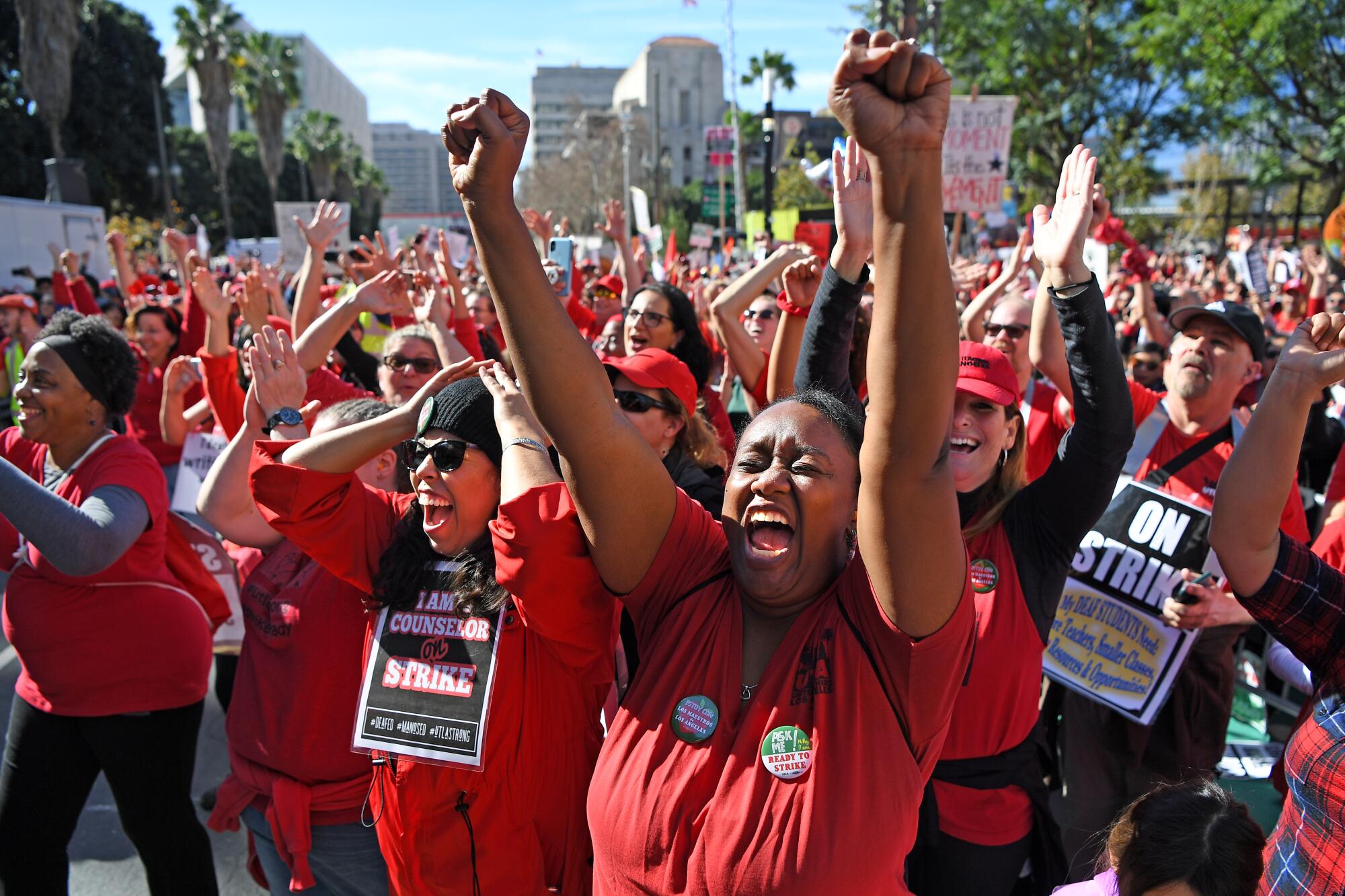 People wearing read and holding sign cheer and raise their hands.