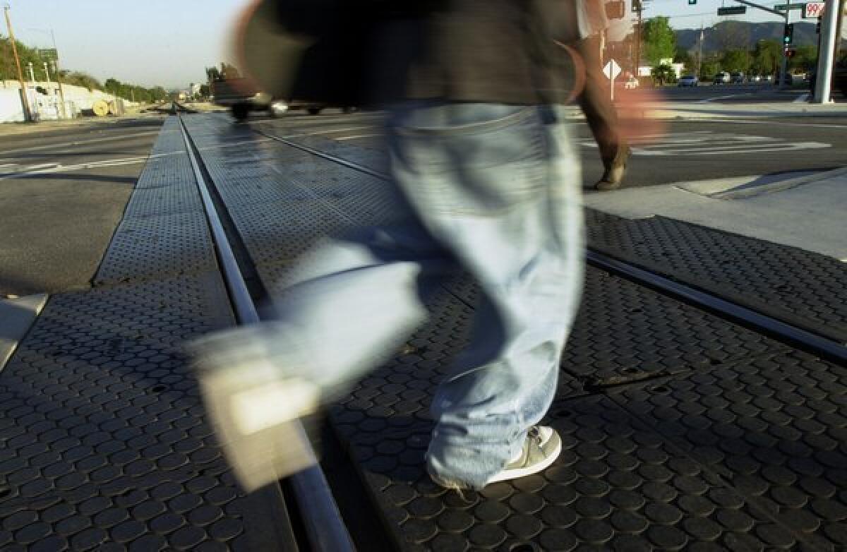 A pedestrian walks across a Metrolink rail at an intersection in Burbank. A person was killed after apparently jumping in front of a train in Orange.