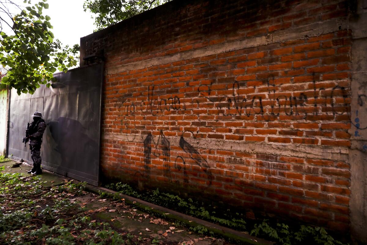 A police officer stands guard next to a graffiti wall with the name of a gang as part of a routine patrol in Lourdes, La Libertad, El Salvador, on Oct. 10, 2019. Human Rights Watch said that at least 138 people deported to El Salvador from the U.S. in recent years were subsequently killed. The new report comes as the Trump administration makes it harder for Central Americans to seek refuge here.