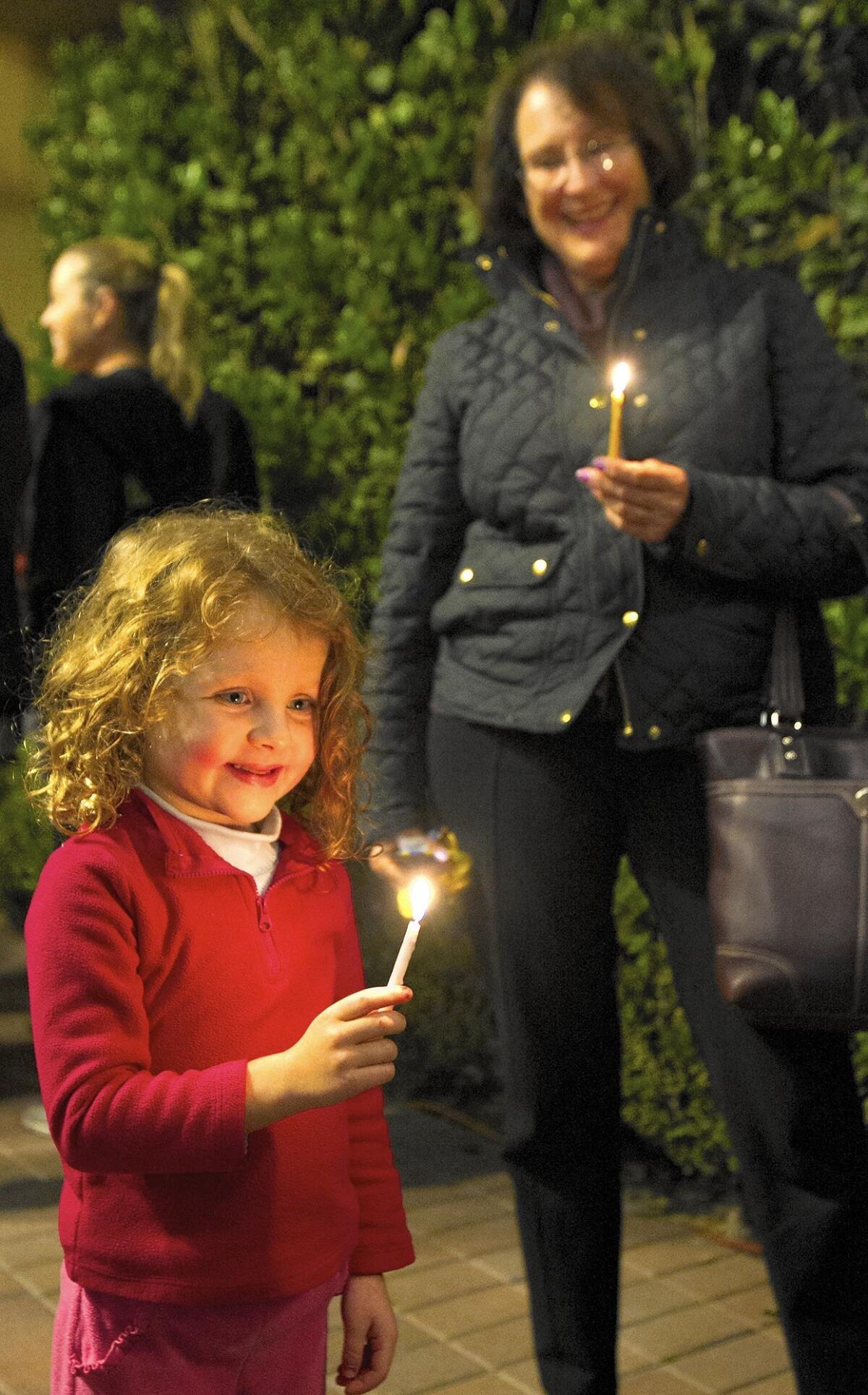 Brooklyn Marcus, left, and Sandra Chakmak hold candles during last year's public menorah lighting at Fashion Island in Newport Beach. This year's Hanukkah commemoration is Sunday at the mall's Atrium Garden Court.