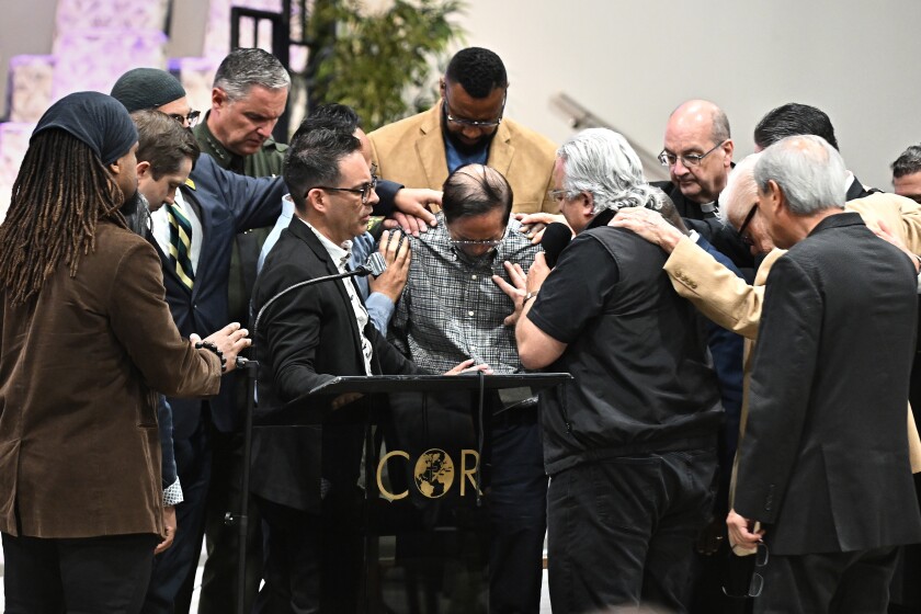 Irvine, California May 16, 2022-Officials pray around former pastor Billy Chang, center, who helped subdue the shooter, tries to hold back his emotions after speaking during a vigil at Christ Our Redeemer Church in Irvine Monday. (Wally Skalij/Los Angeles Times)