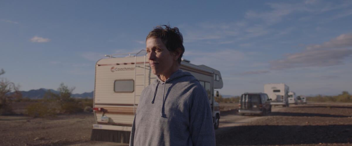 Frances McDormand near a line of mobile homes and a van in the film "Nomadland."